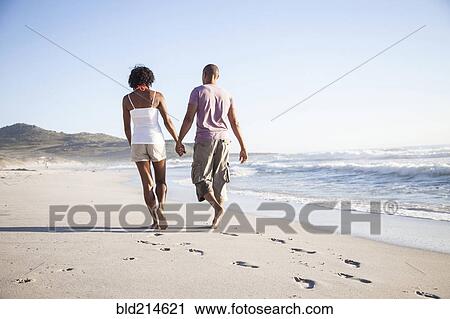 Stock Image - Mixed race couple walking on beach. Fotosearch