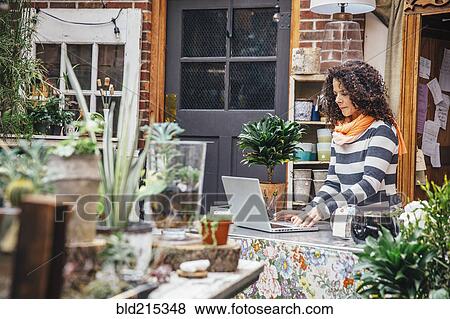 Stock Photo - Mixed race employee using laptop in plant nursery. Fotosearch