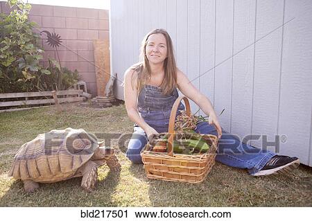 Stock Image - Mixed race farmer and tortoise basket of vegetables. Fotosearch