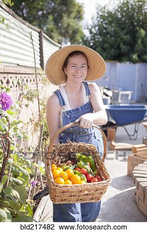Stock Image - Mixed race farmer gathering produce in garden. Fotosearch