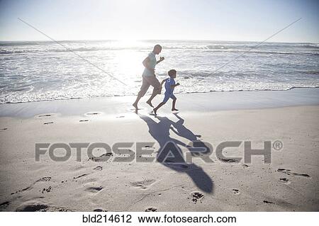 Stock Image - Mixed race father and son running on beach. Fotosearch