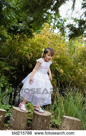 Stock Photo - Mixed race girl balancing on logs in park. Fotosearch