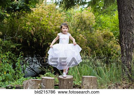 Stock Photograph - Mixed race girl balancing on logs in park. Fotosearch