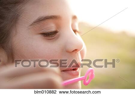 Stock Image - Mixed race girl blowing bubbles. Fotosearch