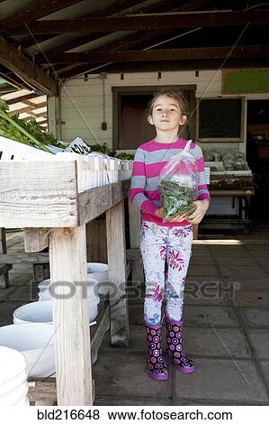 Stock Photo - Mixed race girl holding bag of produce in farmers market. Fotosearch