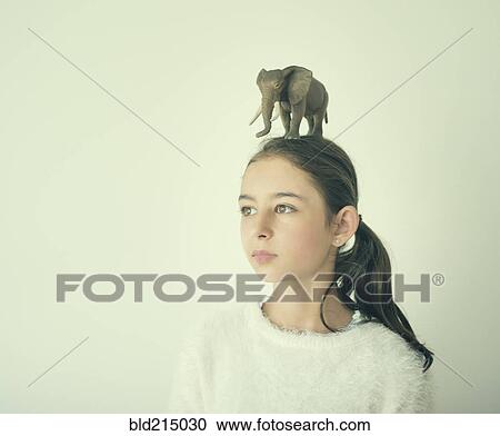 Stock Image - Mixed race girl holding toy elephant on head. Fotosearch
