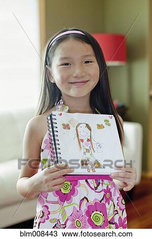 Stock Image - Mixed race girl holding up self-portrait drawing. Fotosearch