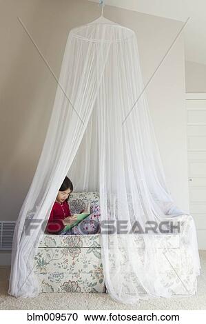 Stock Image - Mixed race girl reading on sofa. Fotosearch