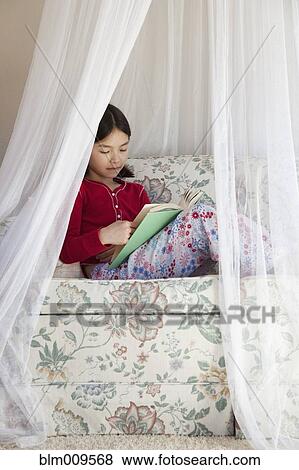Stock Photo - Mixed race girl reading on sofa. Fotosearch
