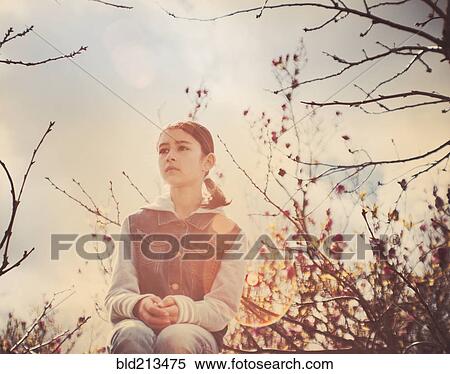 Stock Photography - Mixed race girl sitting in tree outdoors. Fotosearch