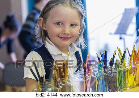 Picture - Mixed race girl smiling near multicolor pencils in classroom. Fotosearch