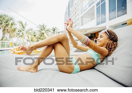 Stock Image - Mixed race girl taking selfie with cell phone on patio. Fotosearch