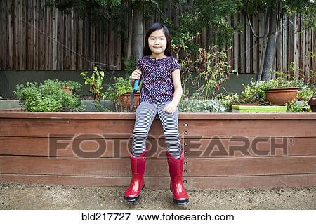 Stock Photo - Mixed race girl wearing rain boots in backyard. Fotosearch