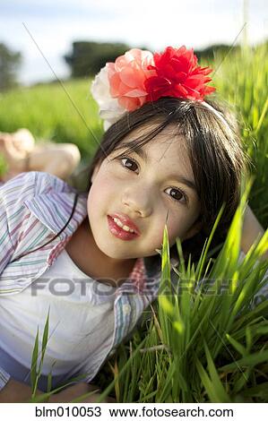 Stock Image - Mixed race girl with flower in hair laying in grass. Fotosearch