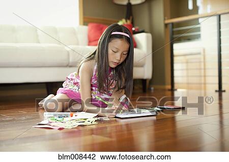 Stock Image - Mixed race girl writing in book on floor. Fotosearch