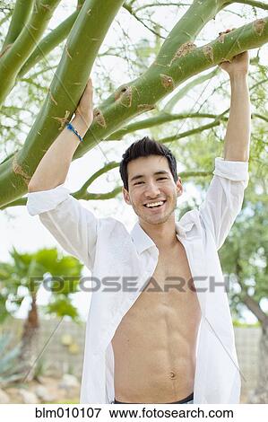 Stock Photo - Mixed race man holding onto tree branch. Fotosearch
