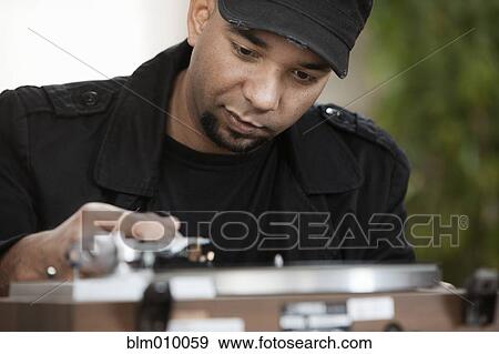 Stock Photo - Mixed race man putting record on turntable. Fotosearch