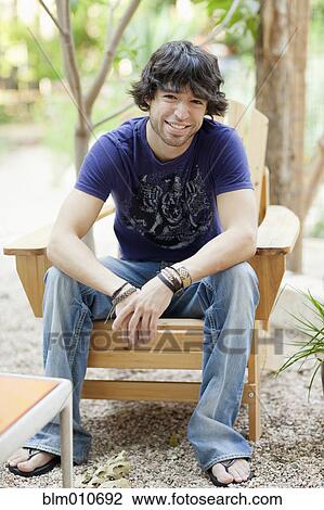 Stock Image - Mixed race man sitting in Adirondack chair. Fotosearch