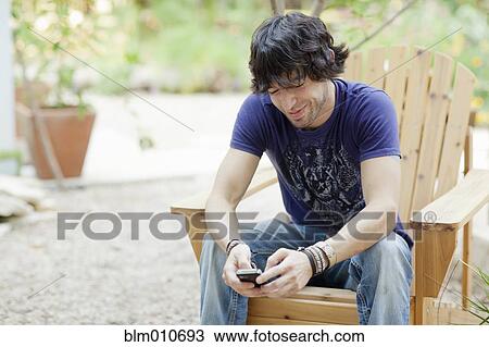 Stock Image - Mixed race man sitting in chair using cell phone. Fotosearch