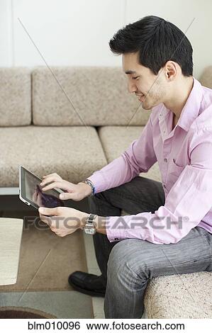 Mixed race man using digital tablet in living room View Large Photo Image Stock Photograph - Mixed race man using digital tablet in living room. Fotosearch