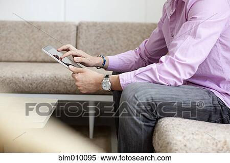 Stock Photography - Mixed race man using digital tablet in living room. Fotosearch