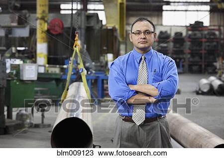Stock Image - Mixed race manager standing in factory. Fotosearch