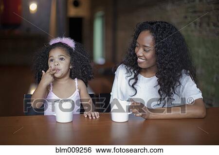 Stock Photograph - Mixed race mother and daughter drinking hot chocolate. Fotosearch