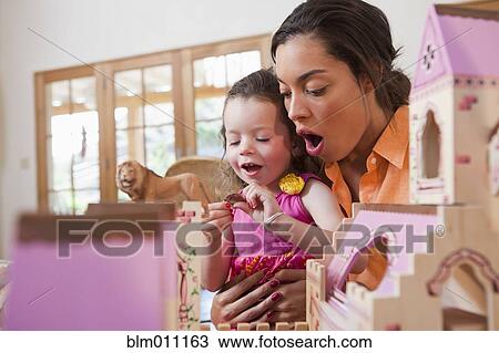 Stock Image - Mixed race mother and daughter playing with dollhouse. Fotosearch