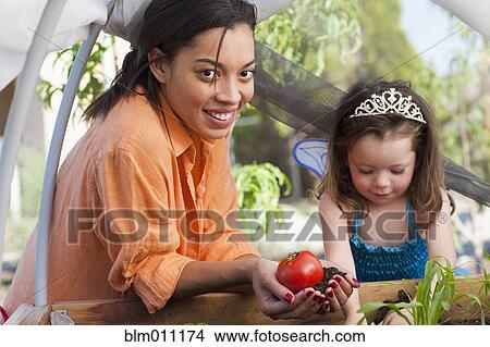 Picture - Mixed race mother and daughter tending garden. Fotosearch