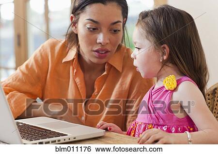 Stock Photograph - Mixed race mother and daughter using laptop. Fotosearch