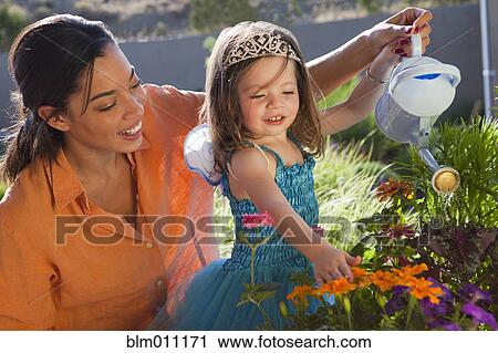 Stock Image - Mixed race mother and daughter watering flowers. Fotosearch