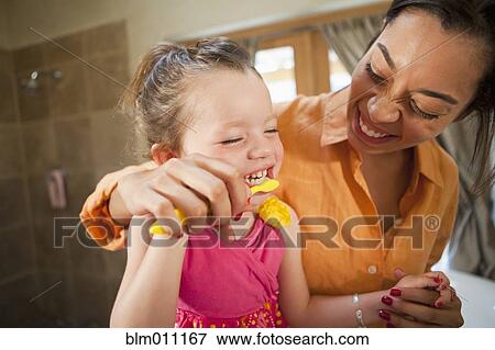 Stock Photo - Mixed race mother helping daughter brush teeth. Fotosearch