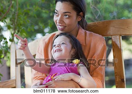 Stock Photo - Mixed race mother holding daughter on lap. Fotosearch