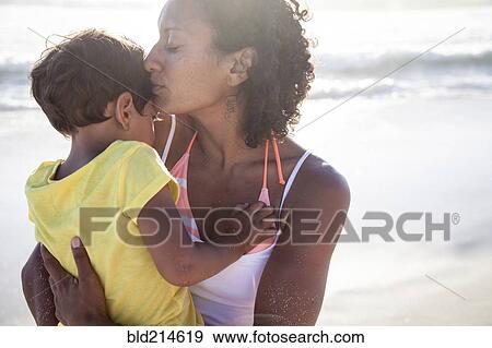 Stock Photo - Mixed race mother kissing daughter on beach. Fotosearch