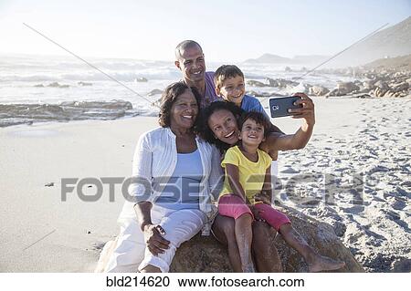 Stock Image - Mixed race multi-generation family taking cell phone selfie on beach. Fotosearch