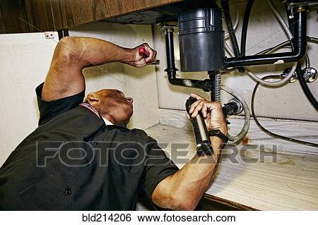 Stock Photograph - Mixed race plumber working under sink. Fotosearch
