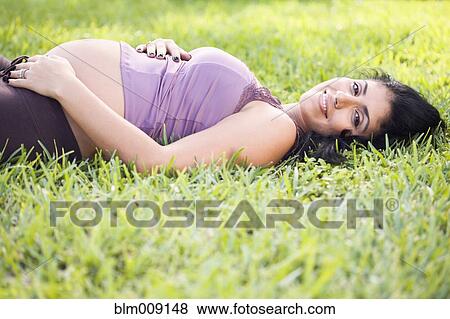 Stock Photo - Mixed race pregnant woman laying in grass. Fotosearch