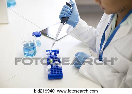 Stock Image - Mixed race scientist pipetting sample into tube in laboratory. Fotosearch