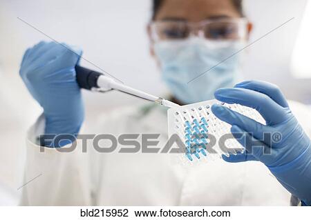 Stock Image - Mixed race scientist pipetting sample into test tube in laboratory. Fotosearch
