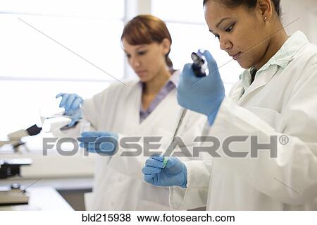 Stock Photo - Mixed race scientists pipetting sample into tube in laboratory. Fotosearch
