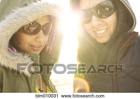 Stock Image - Mixed race sisters in sunglasses and hoods. Fotosearch