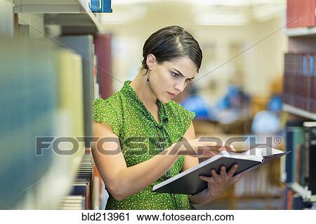 Stock Image - Mixed race student reading book in library. Fotosearch