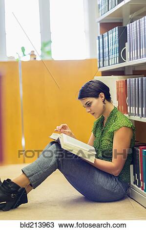 Stock Image - Mixed race student reading book in library. Fotosearch