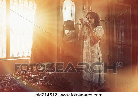 Stock Image - Mixed race woman applying makeup in bedroom. Fotosearch