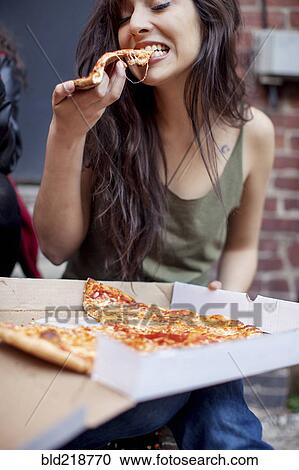 Stock Image - Mixed race woman eating pizza. Fotosearch