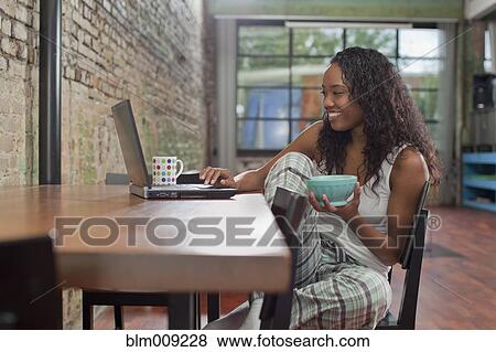 Stock Photo - Mixed race woman having breakfast and using laptop. Fotosearch