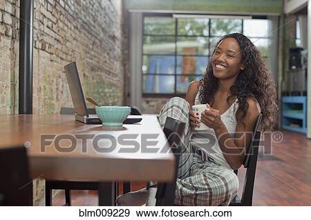 Stock Photo - Mixed race woman having breakfast and using laptop. Fotosearch