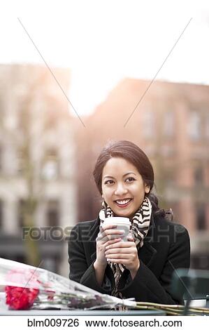 Stock Photograph - Mixed race woman holding coffee with bouquet of flowers. Fotosearch