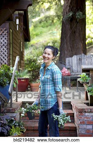 Stock Image - Mixed race woman holding plants in garden. Fotosearch