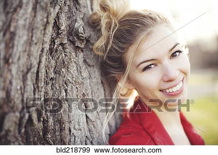 Stock Photo - Mixed race woman leaning on tree trunk. Fotosearch